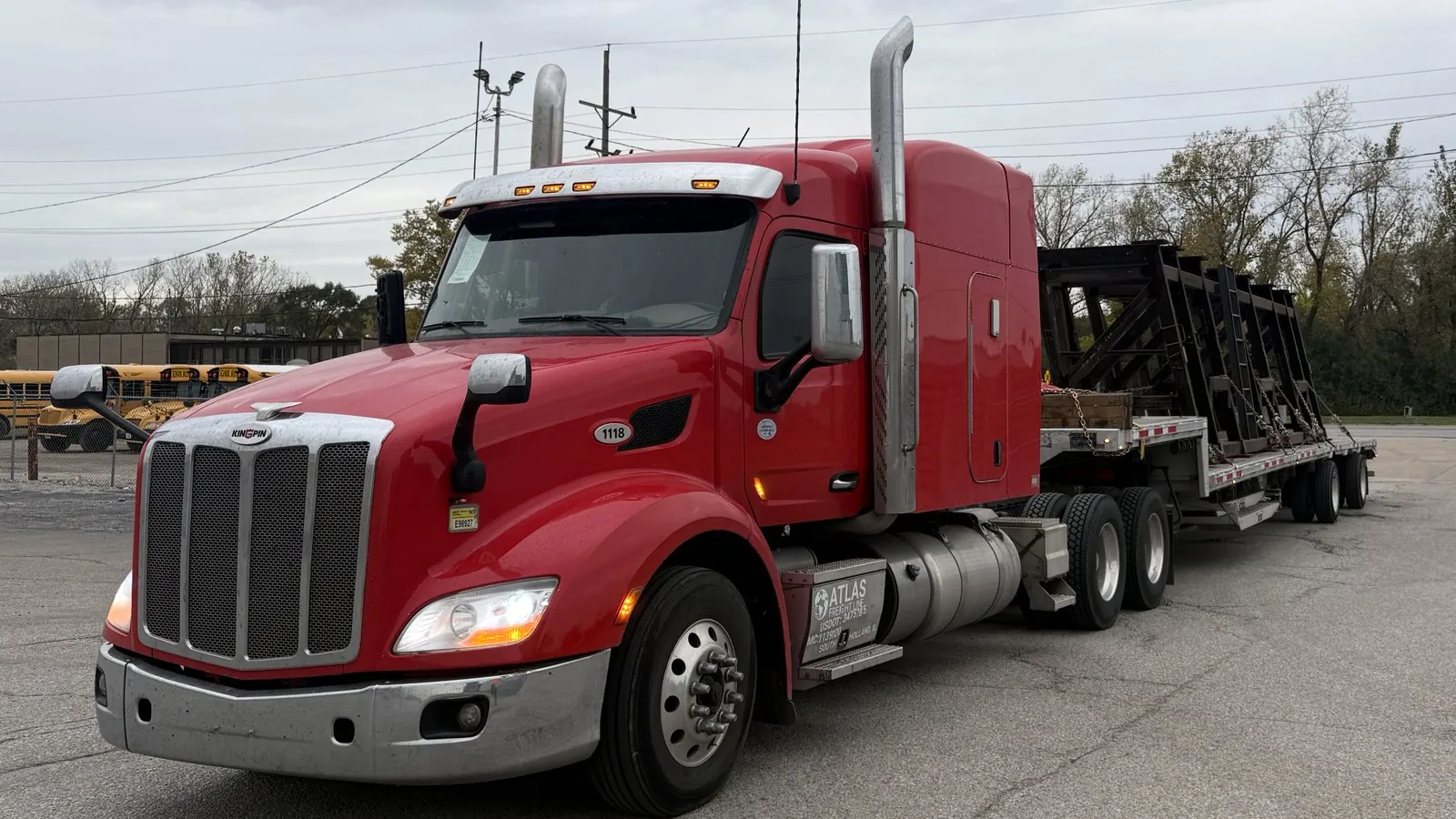 Red Atlas Freight Line Peterbilt pulling a step deck loaded with steel racks